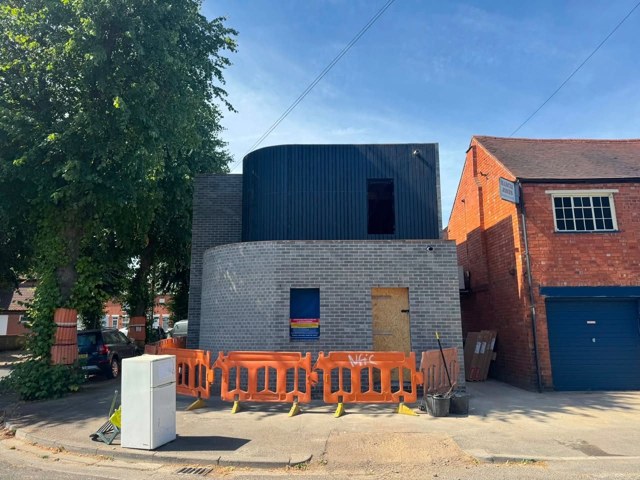 The same curved grey brick building from the corner, showing the curve running round to meet an older red brick building next door