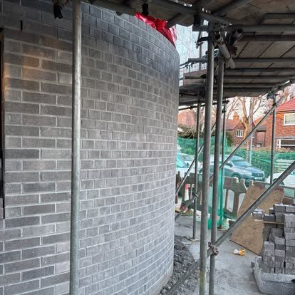 Close view of the curved grey brick wall under scaffolding, showing the courses following the curve