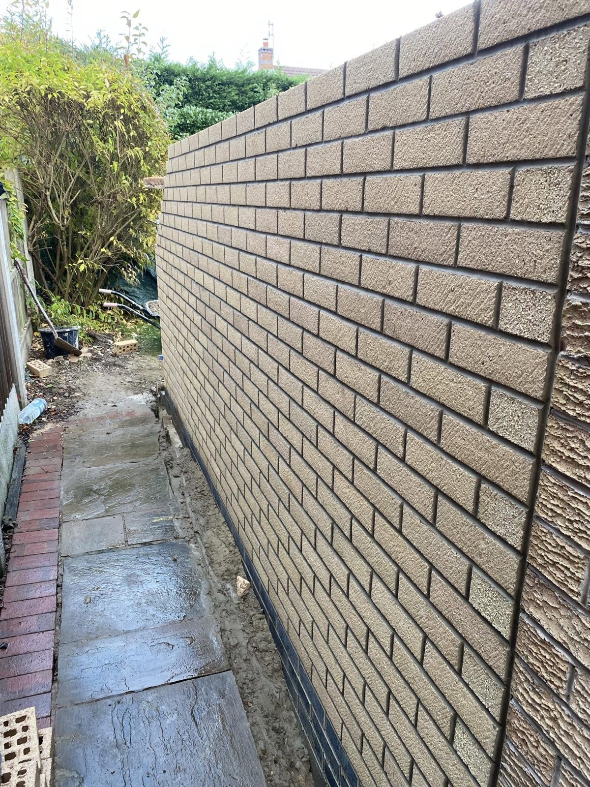 A newly built textured block wall running down the side of a house, with a paved path beside it